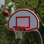 Basketball hoop with ball in mid-air on a sunny outdoor court.