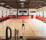 Athlete practicing basketball shots in a spacious indoor gym with wooden flooring.