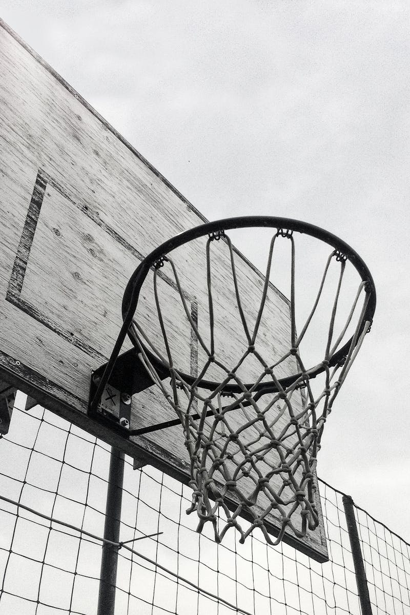 Monochrome shot of a basketball hoop against the sky, capturing the essence of outdoor sports.