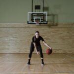 Focused young woman dribbling basketball in indoor court, embodying determination and athleticism.
